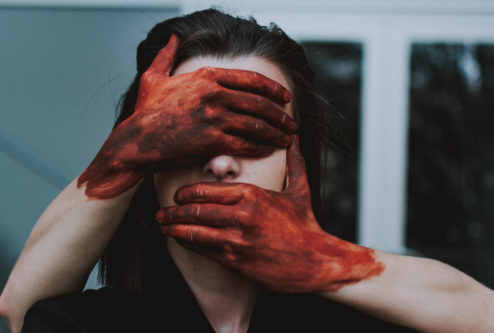 muta la pelle il titolo di questa foto dove due mani sporche di sangue chiudono gli occhi e la bocca di una donna