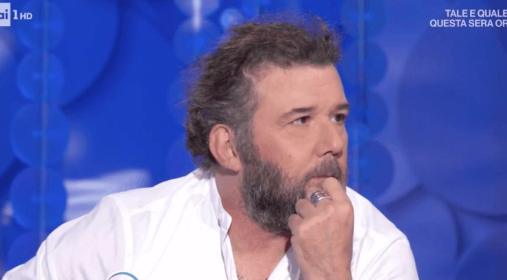 paolo vallesi con la barba, si tocca il mento con la mano sinistra, con aria perplessa