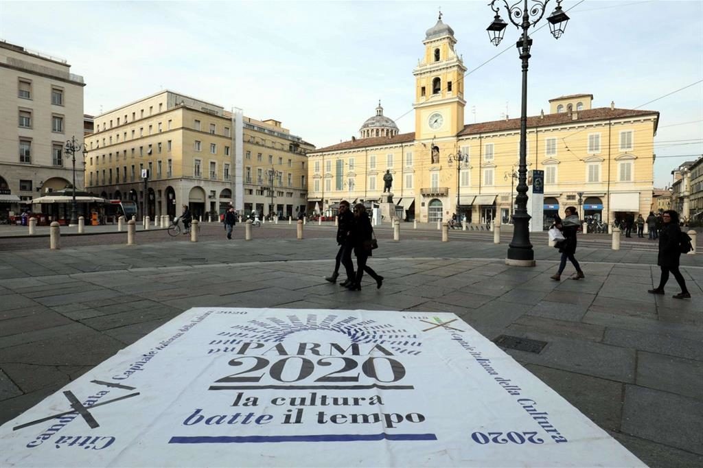 Logo di Parma  su asfalto davanti alla piazza con persone che passano 