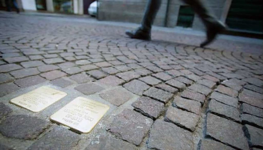 Asfalto con pietre d'inciampo con targa. Piedi che camminano sullo sfondo. 