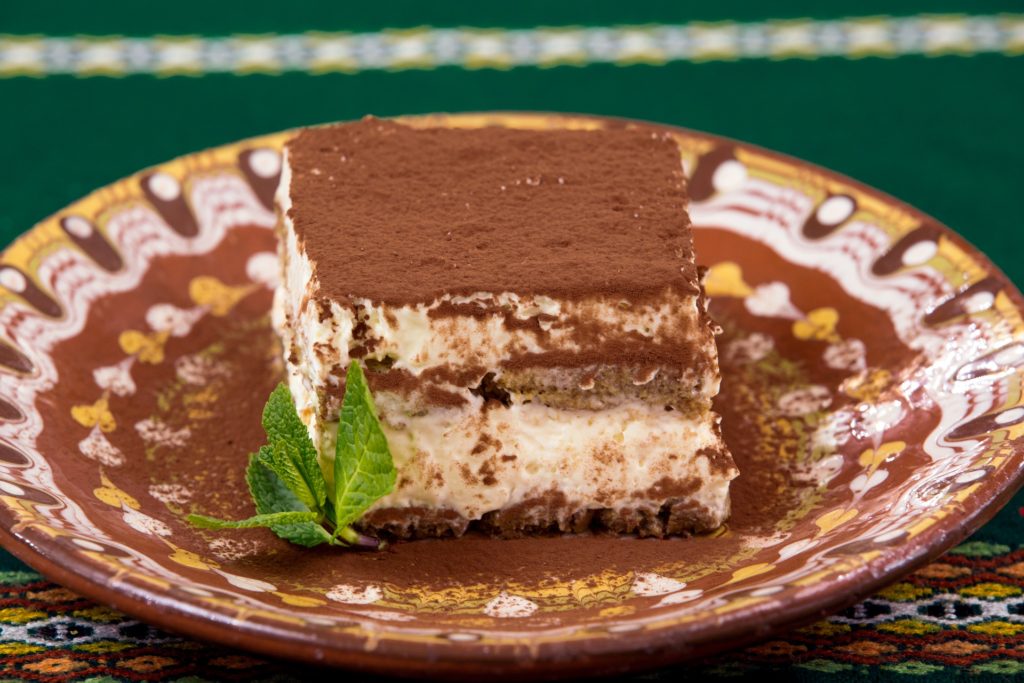 una porzione di tiramisù in un piatto decorato con polvere di cioccolato e una foglia di menta