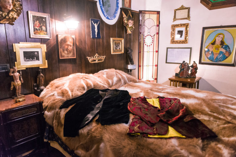una stanza da letto nella casa di Lucio Dalla con tantri quadri appesi ai muri e sul letto dei vestiti dell' artista