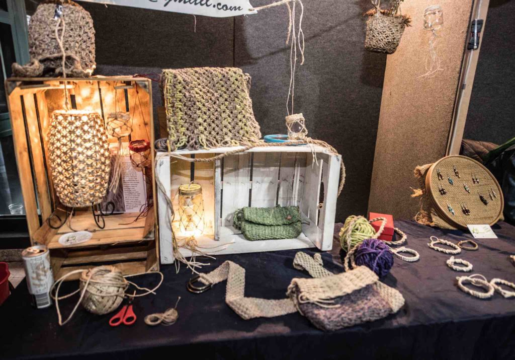 stand della fiera sulla canapa, ci sono diversi oggetti in esposizione al pubblico per la vendita, tra cui collane e braccialetti, borse intrecciate in canapa e altri accessori