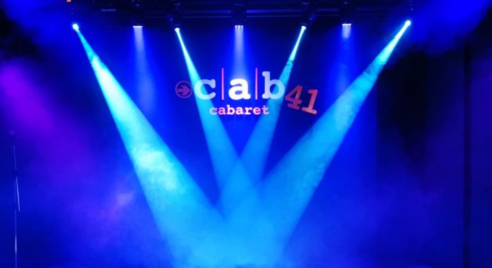 divertimento al cab41 questo weekend, il palco del locale con luci soffuse puntate sul palco, le luci sono di diverse tonalità di blu e azzurro, e c'è anche del fumo da scena, sullo sfondo il nome del cab41