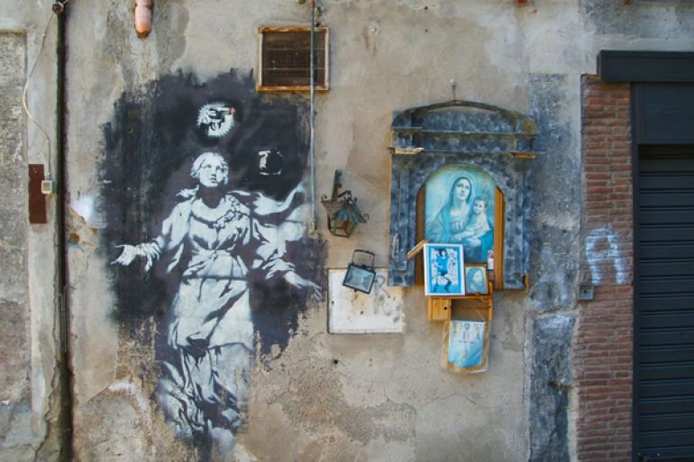 Uno dei murales di Banksy a Napoli. Madonna con la. Pistola al posto dell aureola e edicola votiva a fianco