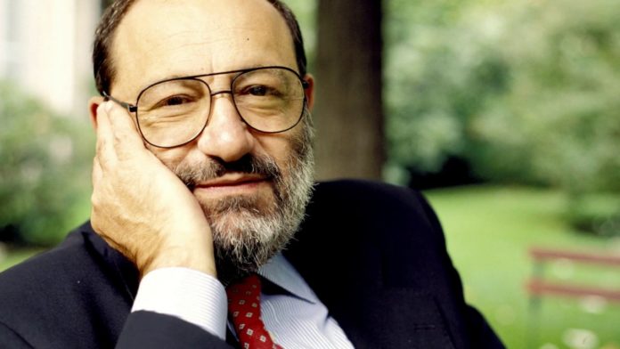 Umberto Eco il nome della rosa, lo scrittore in foto veste gicca scura e cravatta rossa e appoggia il viso sulla mano destra
