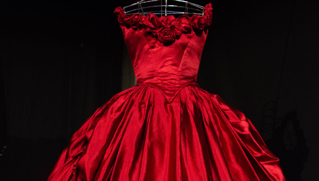 I musei ripartono le aperture straordinarie cinemaddosso la mostra volante di Annamode, rappresentata da un vestito rosso scollato con spalline, con delle rose sul decolletè e ampia gonna lunga