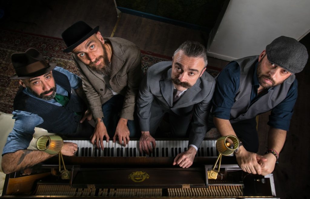 la crew del jerry thomas speakeasy, in ordine da sinistra a destra, alessandro procoli, roberto artusio, antonio parlapiano, e leonardo leuci, suonano tutti insieme un pianoforte, indossano giacca e cravatta, in vestiti eleganti