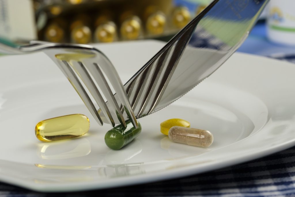 integrazione e alimentazione . delle pillole di vitamine in un piattto e un coltello e forchtaa che simulano di tagliarle