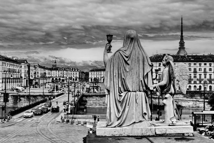 Occhi del Diavolo,città. Fotografia in bianco e nero della città di Torino. Foto scattata dall'altoin cui si vede la Mole Antoneliana. In primo piano, sulla destra, una statua che vede raffigurati un angelo tiene per mano una donna girata di schiena.