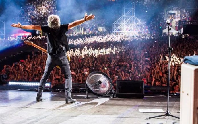 luciano ligabue in tour: primo piano del liga di spalle, sul palco, con le bracciaaperte e la chitarra a tracolla