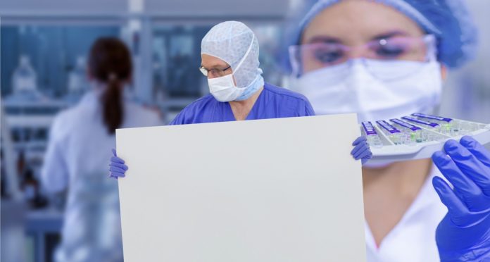 Responsabilità medica ai tempi del Coronavirus un medico tiene in mano un pannello bianco, vicino a lui una donna medico ha in mano un vassoio di provette e sullo sfondo di schiena una donna medico fa delle analisi, tutti sono con la mascherina