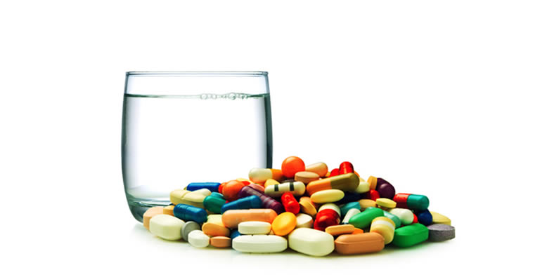 su sfondo bianco, un bicchiere d'acqua con accanto un accumulo di diverse medicine tutte colorate