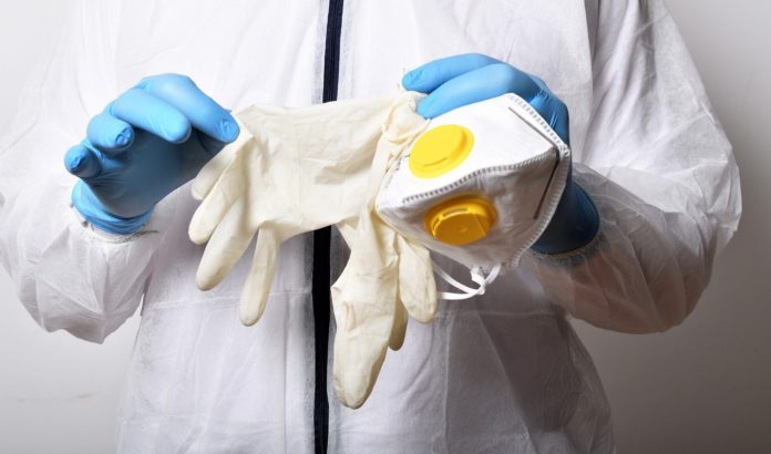 aggiornamenti decreto legge un uomo vestito di bianco con guanti in lattice blu e tra le mani tiene una mascherina sanitaria