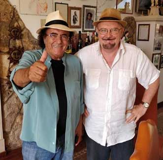 “Terra d’Ambra e di Emozioni” una canzone per la Lettonia interpretata da Al Bano scritta da Charles Goodger. Primo piano dei due artisti: a sinistra al bano che indossa un panama bianco e camicia azzurra, a destra il prof. che indossa una camicia bianca e un cappello di paglia