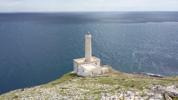 Faro, Punta Palascia. Il Faro di Punta Palascia, di colore bianco, circondato da una vasta vegetazione e dal mare.