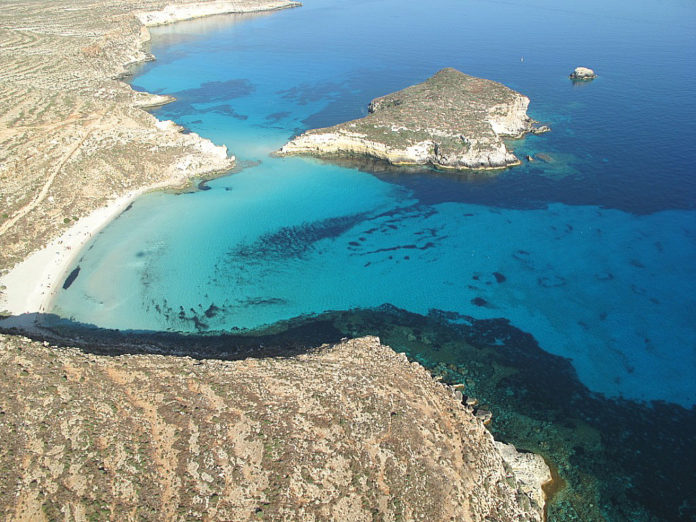 Isola dei Conigli, Lampedusa. Il mare di colore azzurro chiaro con macchie blu, circondato da rocce di colore marrone chiaro.