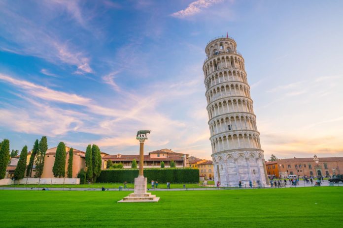La Torre di Pisa, pendente. La Torre, simbolo di Pisa, di colore bianco. Il paesaggio raffigura un prato verde chiaro e il cielo azzurro con striature bianche.