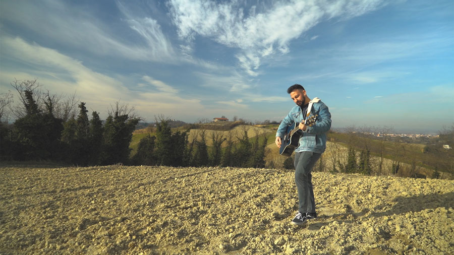 “Non fatemi smettere di sognare” segna l’esordio assoluto di Leone. nella foto il cantautore all'aperto, su una collina, con addosso jeans, giubbotto di jeans, e la chitarra acustica a tracolla