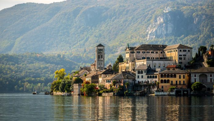 Orta San Giulio, borgo. Il borgo si affaccia sul Lago D'Orta. Sullo sfondo alberi di colore verde scuro, mentre il colore dell'acqua riflette le case.