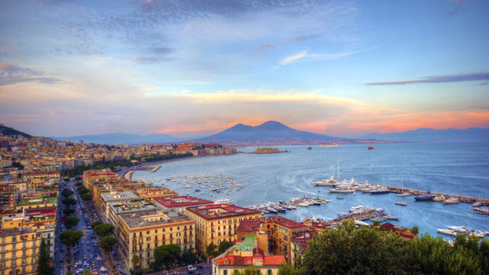 Posillipo. Napoli al tramonto, con il mare circondato da case e sullo sfondo l'imponente Vesuvio.