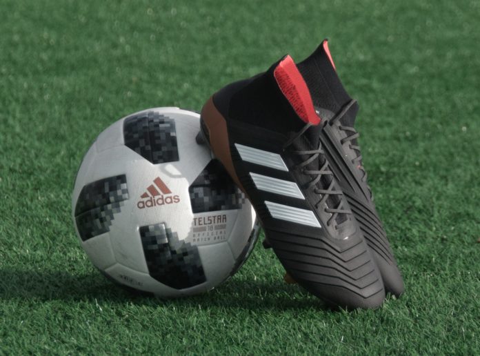 Davvero riprende il campionato di Serie A? Davvero torneranno le partite? Davvero interessa ancora? Primo piano di un paio di scarpe da calcio adidas, appoggiate ad un pallone bianco e nero, su un campo da calcio