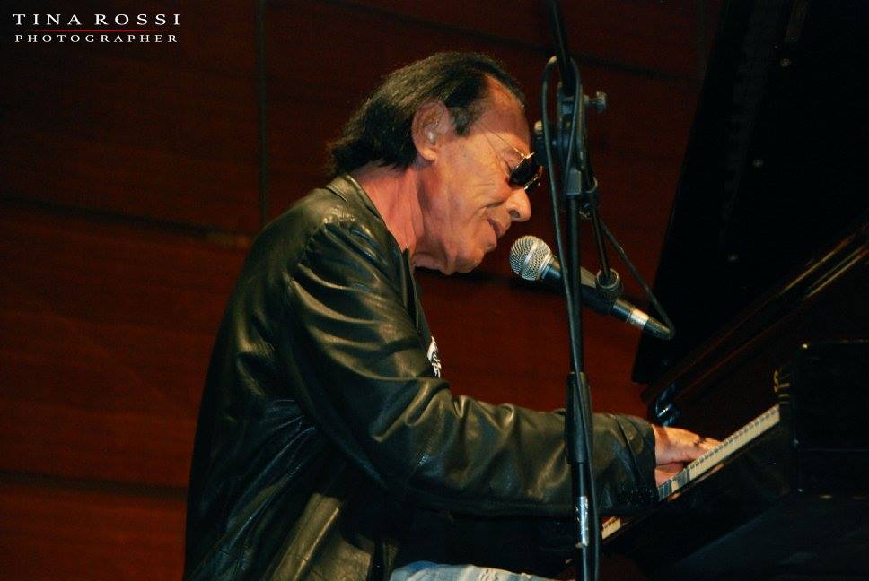 Antonello Venditti, nella notte di roma. Nella foto il cantante seduto al pianoforte, intento a suonare, che indossa una giacca di pelle nera