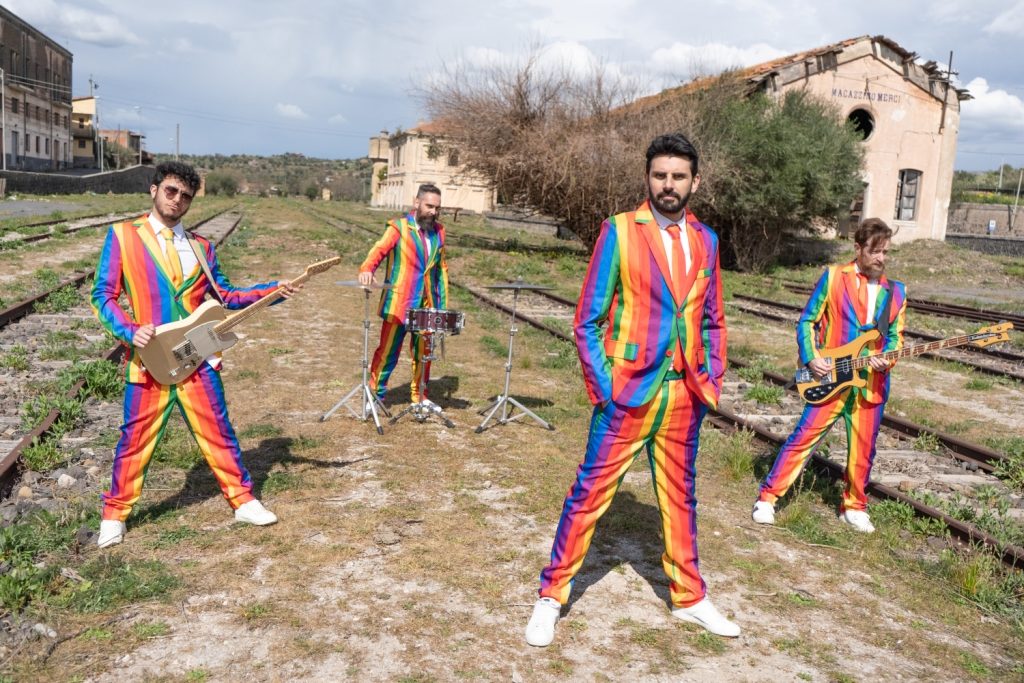 “Il geghegè” l’omaggio dei Camera a Sud a Rita Pavone. Nella foto la band siciliana, all'aperto, sui binari di una ferrovia, e i membri che indossano abiti a strisce colorate