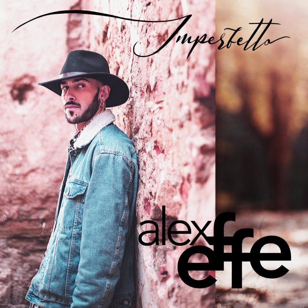 imperfetto il nuovo singolo di Alex Effe. nella foto il cantante, appoggiato a un muro di mattoni, che indossa cappello nero da cawboy, e giubbotto di jeans con il colletto di pelliccia