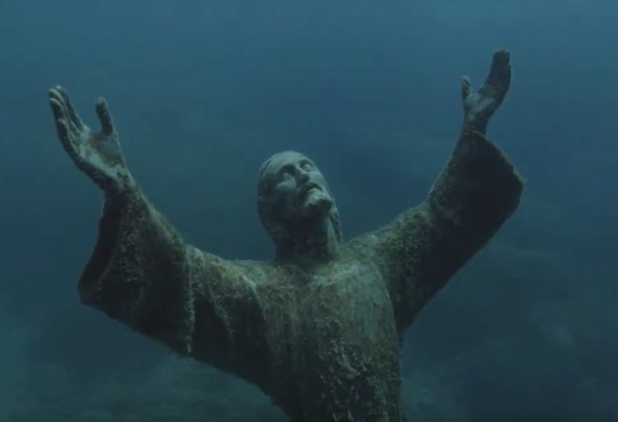Povero Dio il Cristo degli abissi con La statua di Gesu con le braccia eil viso rivolto verso l'alto sommerso nel mare