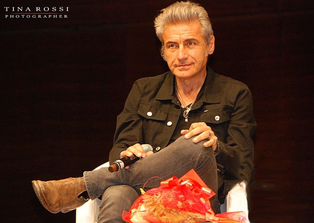 SalTo Rewind: Luciano Ligabue “Scusate il disordine”. Nella foto il "Liga" vestito con pantaloni e camicia di jeans marroni, con le gambe accavallate, seduto su una sedia con il miscrofono in mano