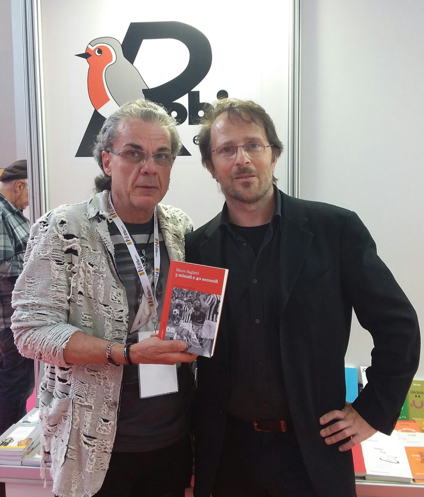 3 minuti e 40 secondi mauro saglietti, nella foto insieme a lele boccardo, a sx che ha il libro in mano e inossa una giacca di cotone grigia, l'autore a dx vestito di nero