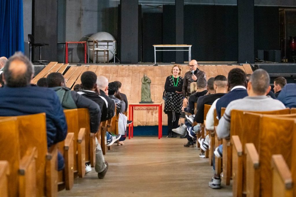 evasione dell'arte nella foto una sala con delle persone sedute e due oratori