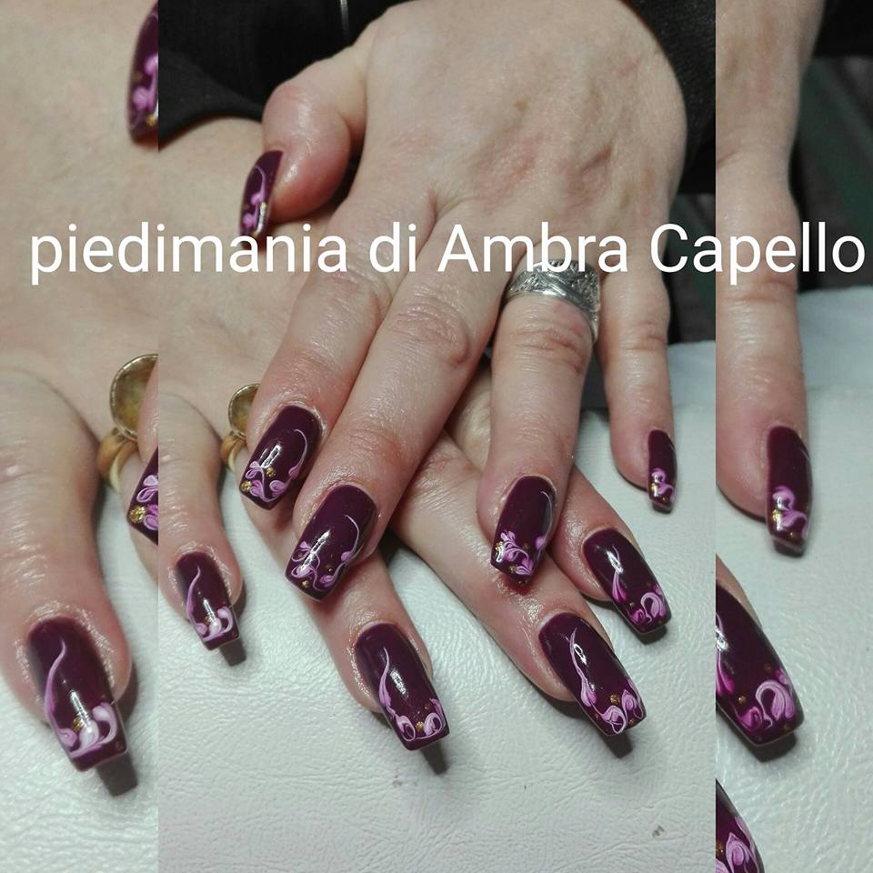 centri estetici e nail art - nella foto delle mani da donna con delle unghie lunghe smaltate di rosso scuro con disegni dipinti