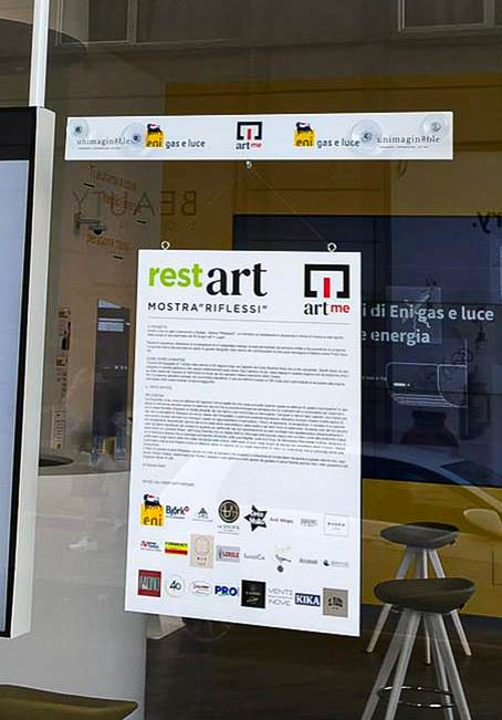 La locandina di Restart la mostra di ArtMe esposta sulla vetrina di un negozio eni store