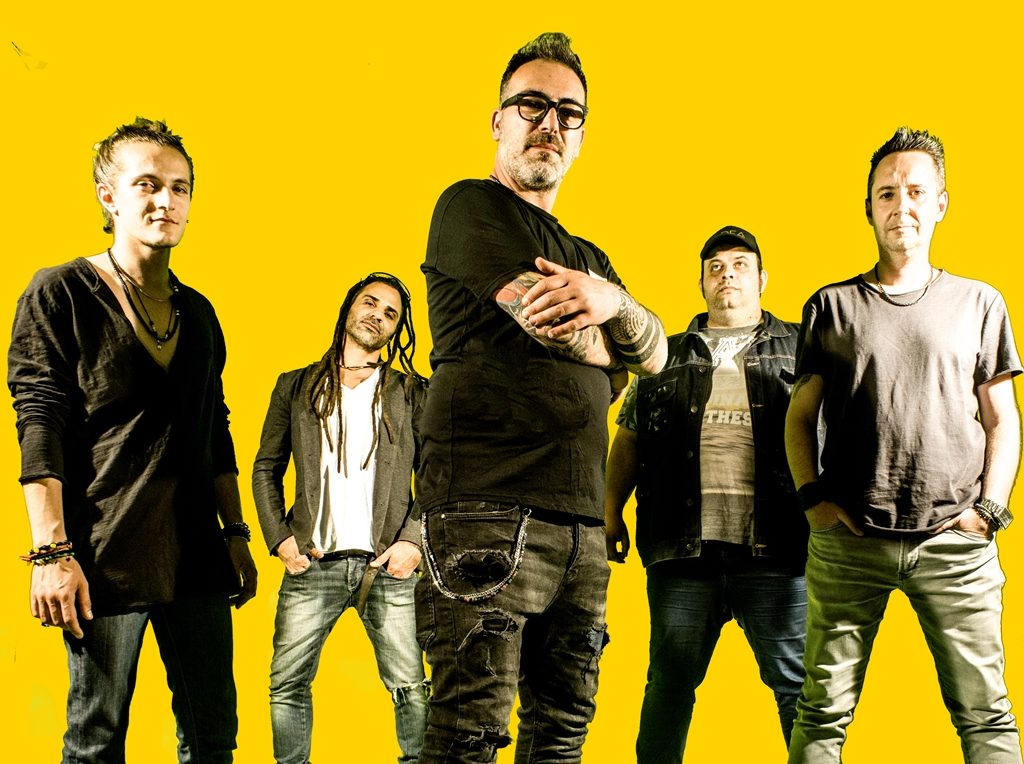 “Umani” è il titolo del nuovo album degli I-Dea. nella foto i cinque componenti della band torinese, davanti  uno sfondo giallo