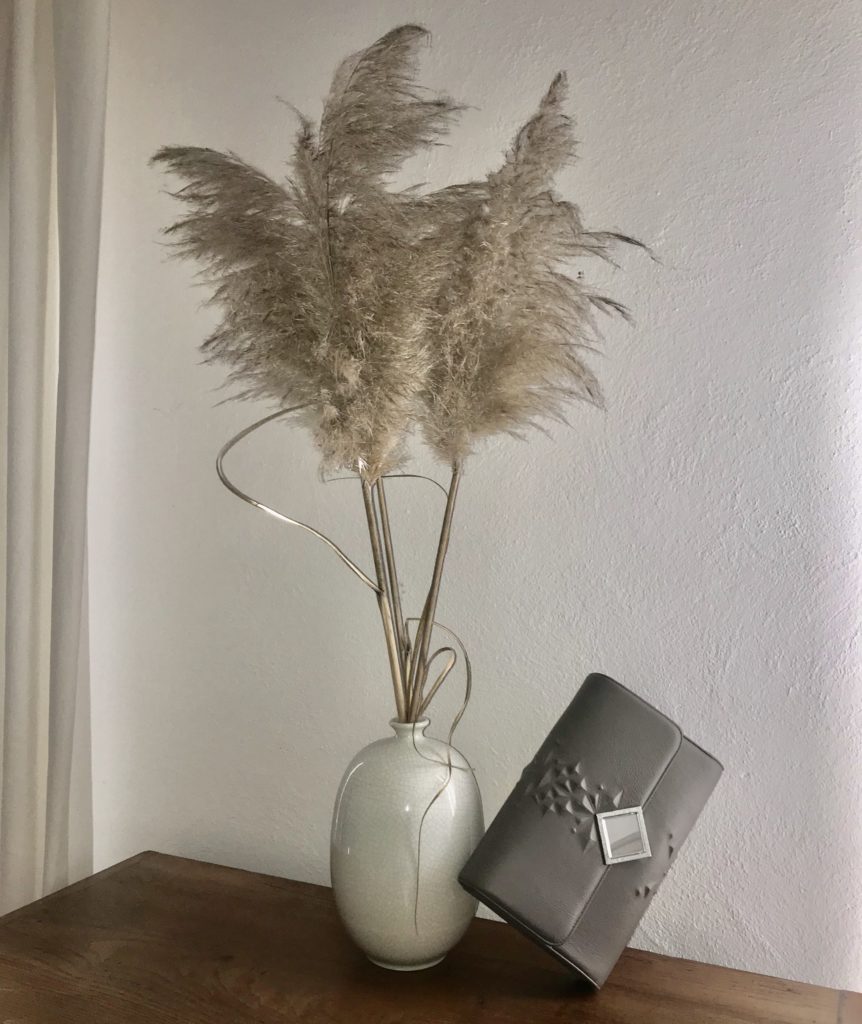 Virginiamaina accessori: una borsetta appoggiata vicino ad un vaso bianco con delle piume