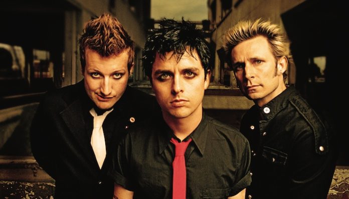Nella foto i tre componenti della band dei Green Day, in camicia nera. Da sinistra Tré Cool con la cravatta bianca, Billie Joe Armstrong con la cravatta rossa e ultimo Mike Dirnt solo con la camicia nera, guardano davanti a loro. Billie Joe ha gli occhi truccati con la matita nera.