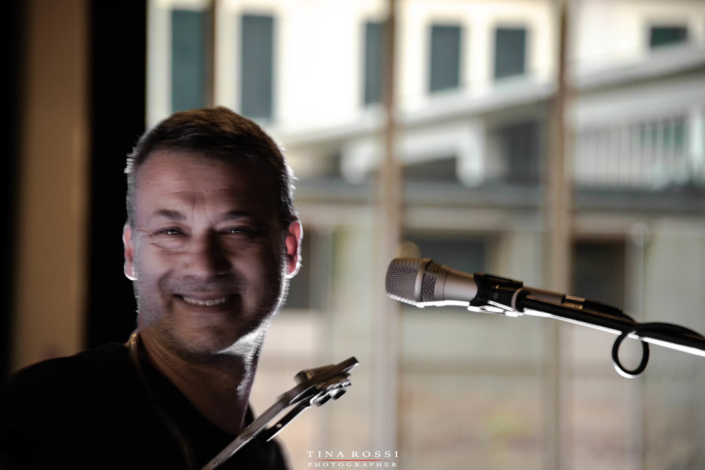 Alex D'Herin in un primo piano sorridente con un mixrofono sulla destra