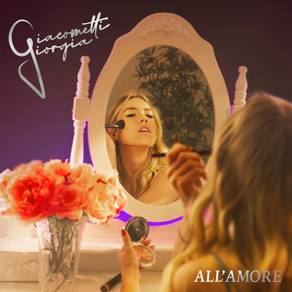 Giorgia Giacometti all'amore. La copertina del singolo che ritrae la bionda cantante davanti ad uno specchio intenta a truccarsi, sulla destra un vaso di vetro con dei fiori rossi