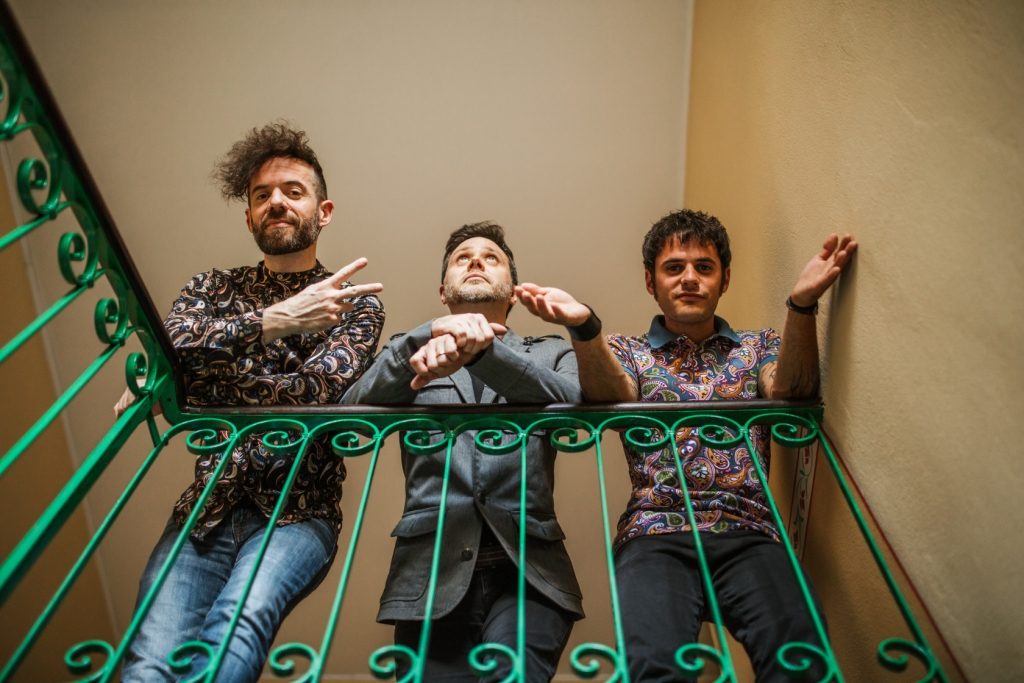 The Monkey Weathers  "matilda". Nella foto i tre ragazzi della band, che indossano camicie a fiori, appoggiati a una ringhiera, su un pianerottolo