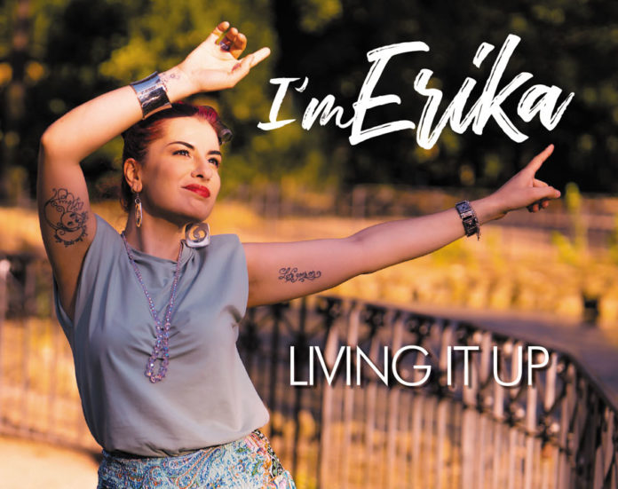 Im erika - living it up la copertina del nuovo singolo, che ritrae la cantante con le braccia alzate, una gonna colorata e una t-shirt grigia senza maniche. Ha i capelli rossi raccolti sulla nuca e sorride.