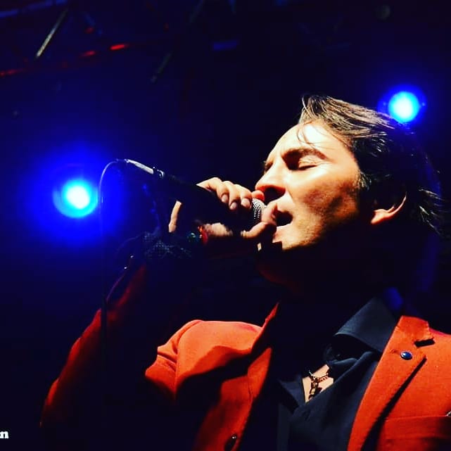 mojito d'ariaa feat edel farias. nella foto il cantante argentino col microfono in mano, indossa una giacca rossa e camicia nera