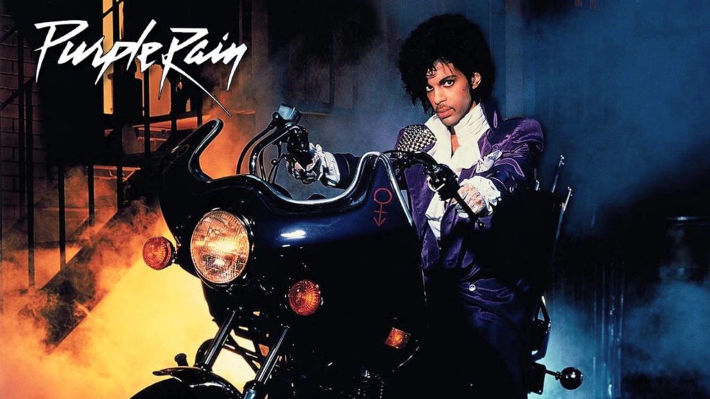 purple rain prince. la copertina del disco, che ritrae il cantante americano, giacca viola e camicia bianca, in sella a una moto nera