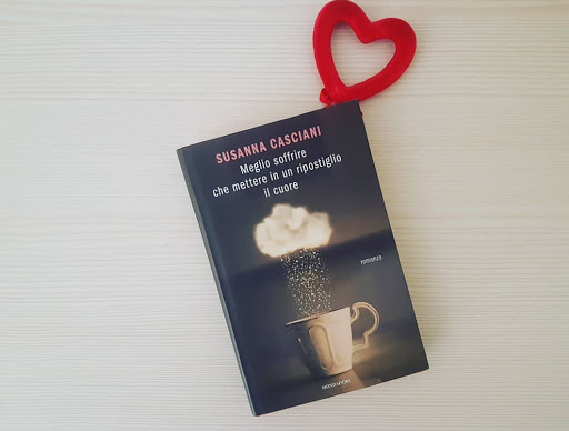 Meglio soffrire che mettere in un ripostiglio il cuore, romanzo, Susanna Casciani. Il romanzo in primo piano. La copertina presenta il titolo di colore bianco e il nome della scrittrice in rosa. Sulla copertina è rappresentata una nuvola da cui cade pioggia con sotto una tazza di colore bianco.