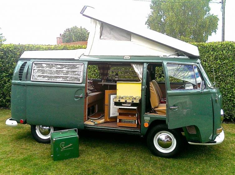 Vacanze in camper - nella foto il vecchio modello della Volkswagen verde con tetto estensibile , aperto sul fianco adibto all'interno con letti e cucina