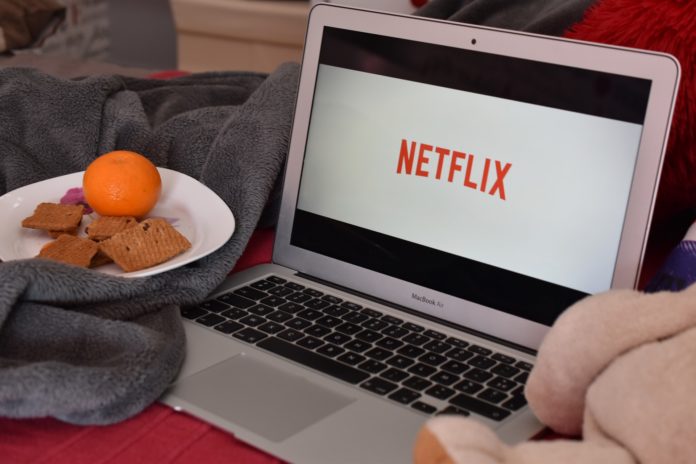 Account Netflix - la schermata della piattaforma TV su un computer e di fianco un piattino con biscotti e un arancio