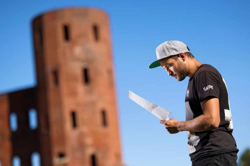 Saype , l'artista che affresca l'erba, e il suo "abbraccio" a Torino alle Porte Palatine. artista con cappellino davanti a i muri