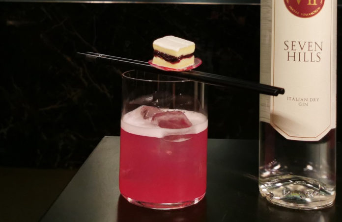 The pink hill è il nome del drink nella foto,di colore rosso servito in un bicchiere tumbler con due bacchette cinesi appogiate sopra e sopra le bacchette un piccolo quadrato di tramezzino