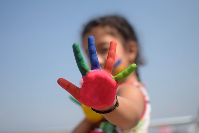 Violenza sulle donne - una bambina con una mano tesa e aperta con le dita e il palmo colorate